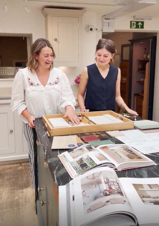 two women inside a kitchen showroom looking at samples with open books