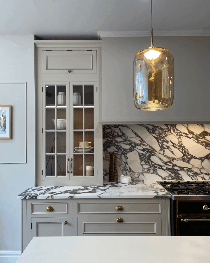 A modern kitchen featuring neutral cabinetry, marble countertops with a unique veining pattern, and a stylish glass pendant light.
