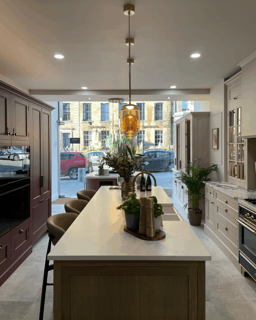 Interior view of a stylish kitchen showroom featuring a central island, modern appliances, and pendant lighting, with a view of a street through the front window.
