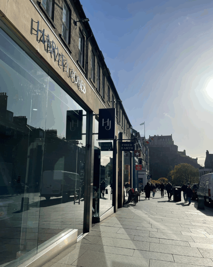 Sunlit view of the Harvey Jones Edinburgh showroom on a city street with pedestrians, parked vehicles and view of Edinburgh Castle
