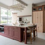 Luxury kitchen design with blush cabinetry, burgundy island and walnut tall units.
