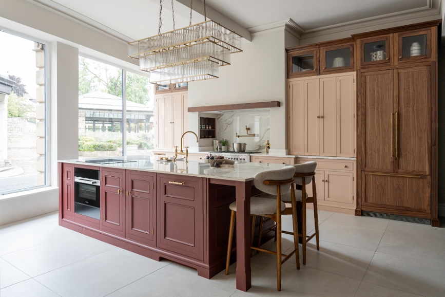 Luxury kitchen design with blush cabinetry, burgundy island and walnut tall units.