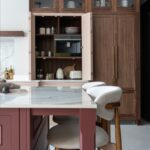Open blush and walnut larder beside island seating in a luxury kitchen design.