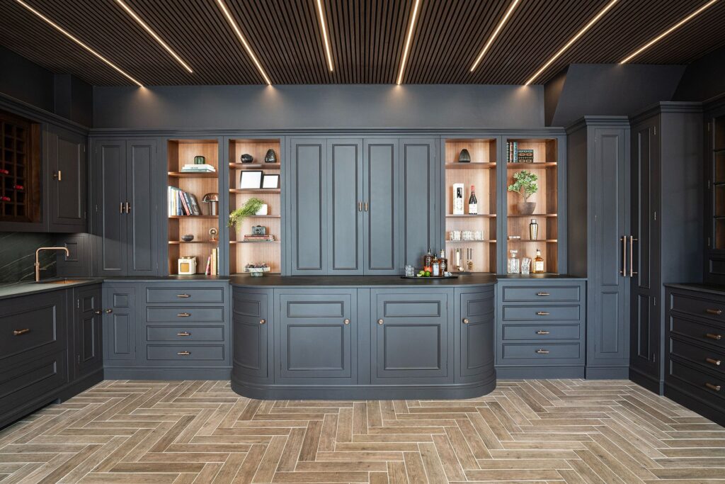 Full wall of dark bespoke kitchen cabinetry with illuminated timber shelving and curved center cabinets.