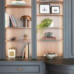 Illuminated open shelving in a dark kitchen with warm wood interiors and decorative accessories.