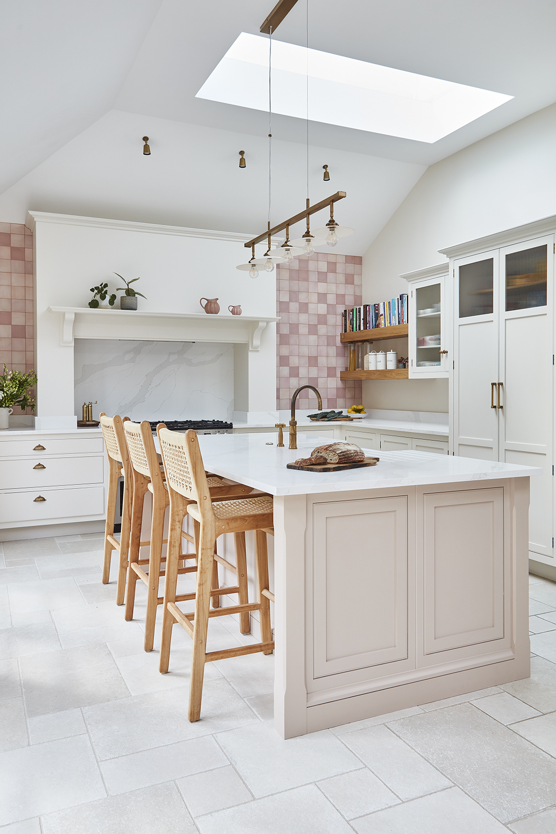 Soft pink kitchen design with wooden island seating and tall skylight