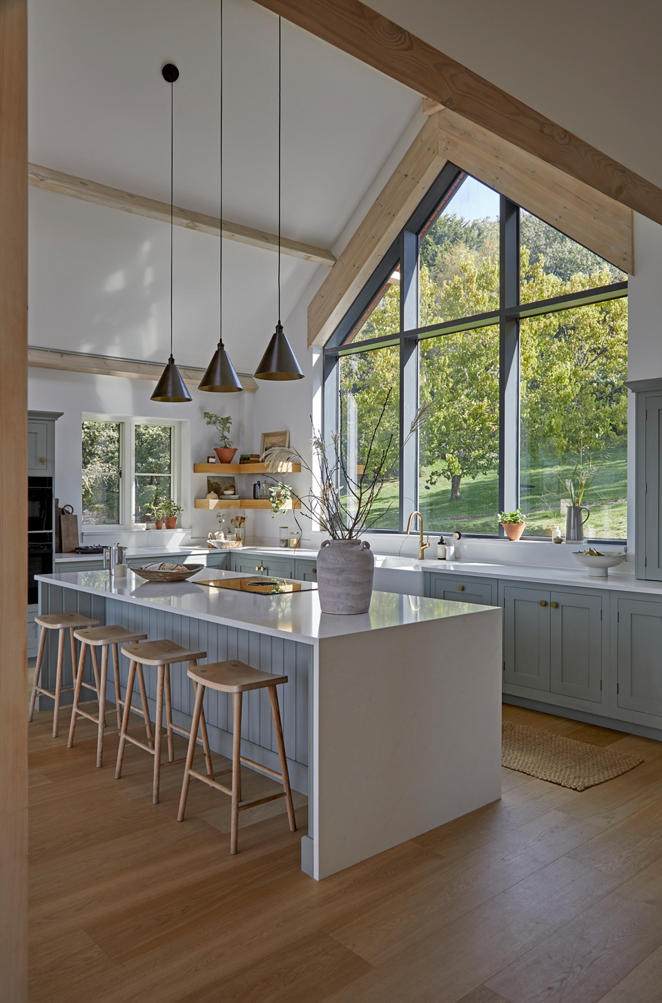 Bright light blue Shaker kitchen with island, natural wood details and gable end window.