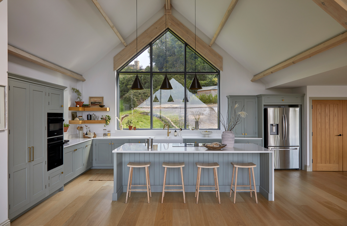 Large trapezium gable window flooding the blue kitchen with natural light.