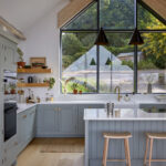 Panelled island seating in a blue Shaker kitchen with light wood stools.
