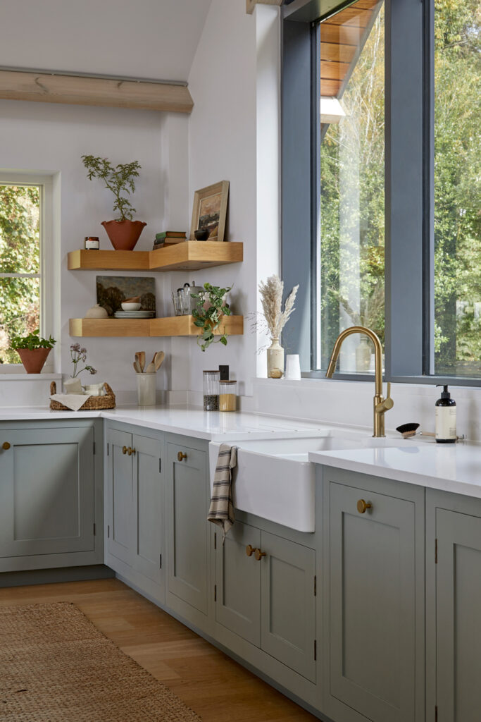 Open wooden shelving in a light blue Shaker kitchen with bespoke design displaying plants and ceramics.