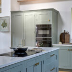 Integrated double ovens within tall Shaker cabinetry in a light blue kitchen