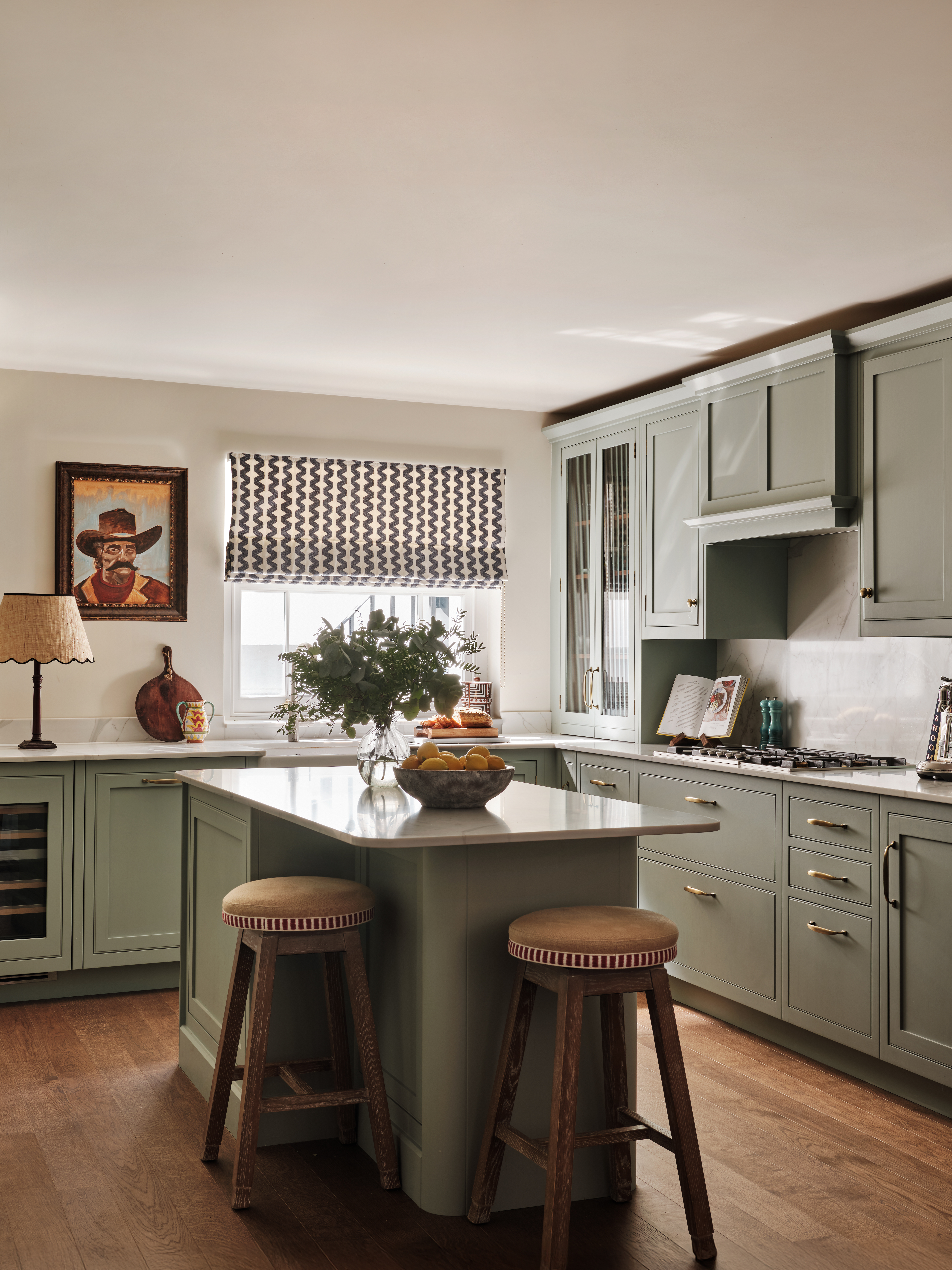 Sage green kitchen with bespoke kitchen island, marbled quartz worktop and rustic wooden stools.