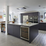 Bespoke navy kitchen island with wine fridge, recipe book shelving and oak worktop seating area.
