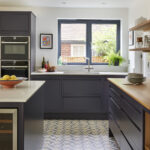Modern open plan kitchen with navy units, oak accents and geometric yellow and navy tiled floor detail.
