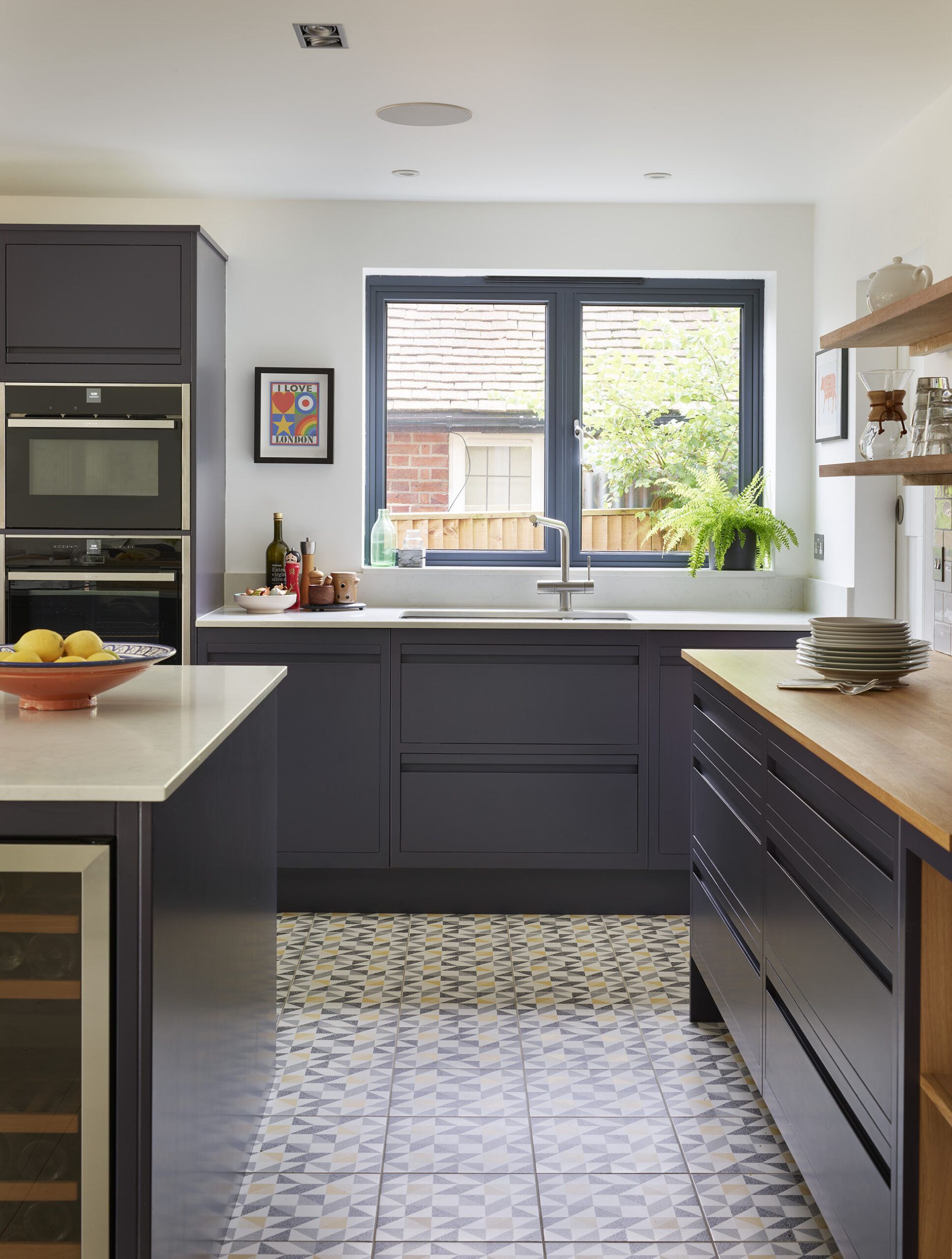 Modern open plan kitchen with navy units, oak accents and geometric yellow and navy tiled floor detail.