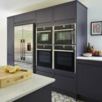Integrated double ovens and space for a double fridge freezer within navy handleless kitchen cabinetry.
