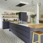 Luxury open plan kitchen with navy cabinetry, patterned floor tiles and sleek ceiling mounted extractor fan.