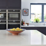 Navy kitchen island with full height kitchen cabinetry with handleless drawers and built in double ovens in a sleek Linear Edge design.