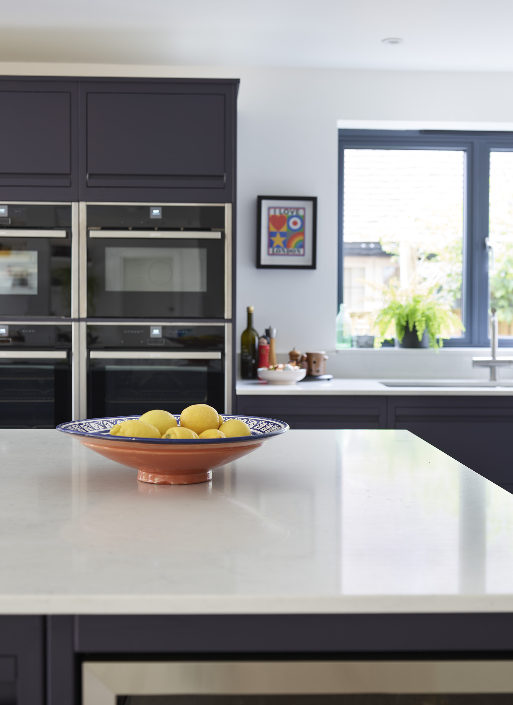 Navy kitchen island with full height kitchen cabinetry with handleless drawers and built in double ovens in a sleek Linear Edge design.