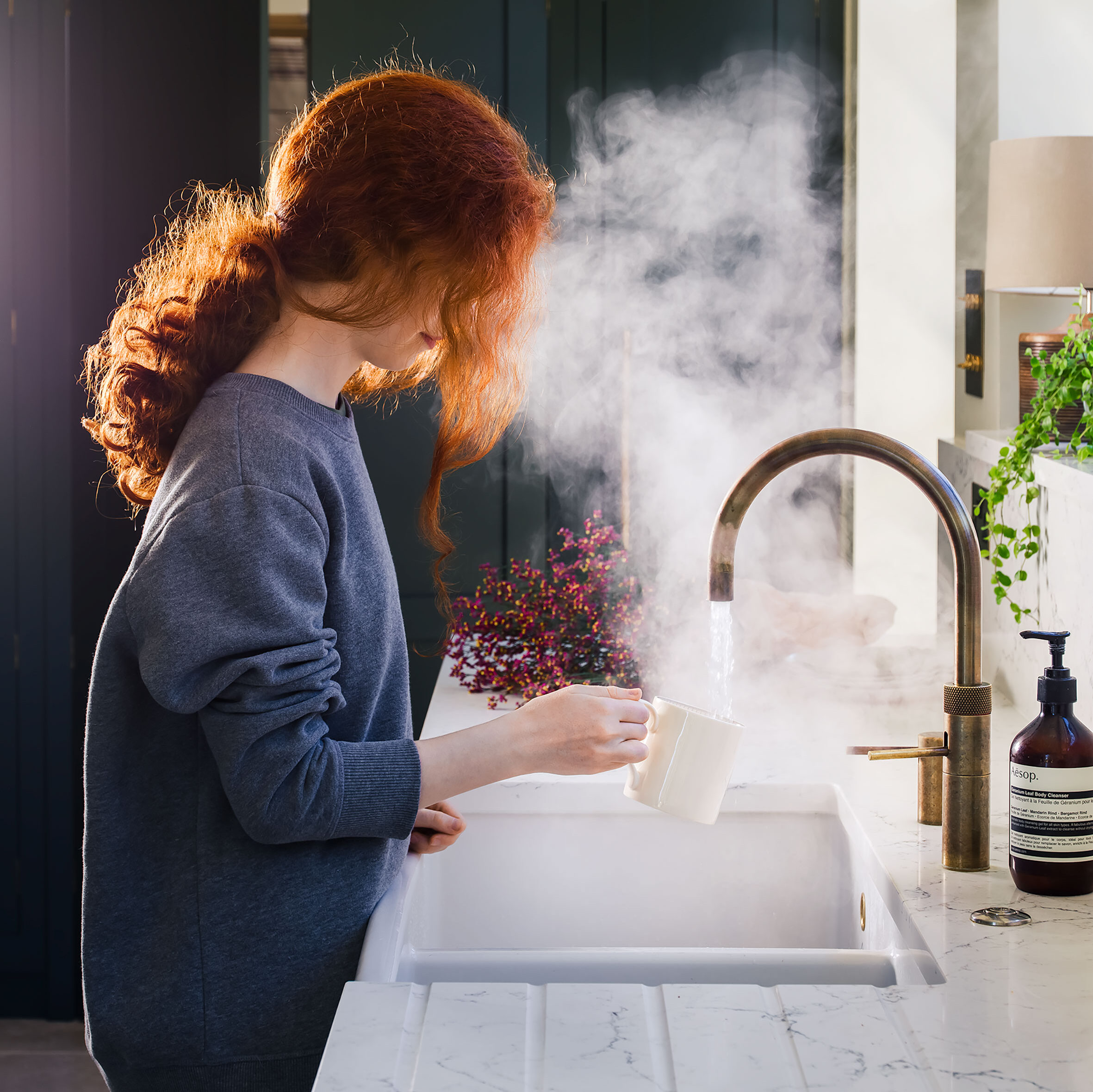 girl stood at a counter top using a boiling tap with steam coming from the water falling into a mug