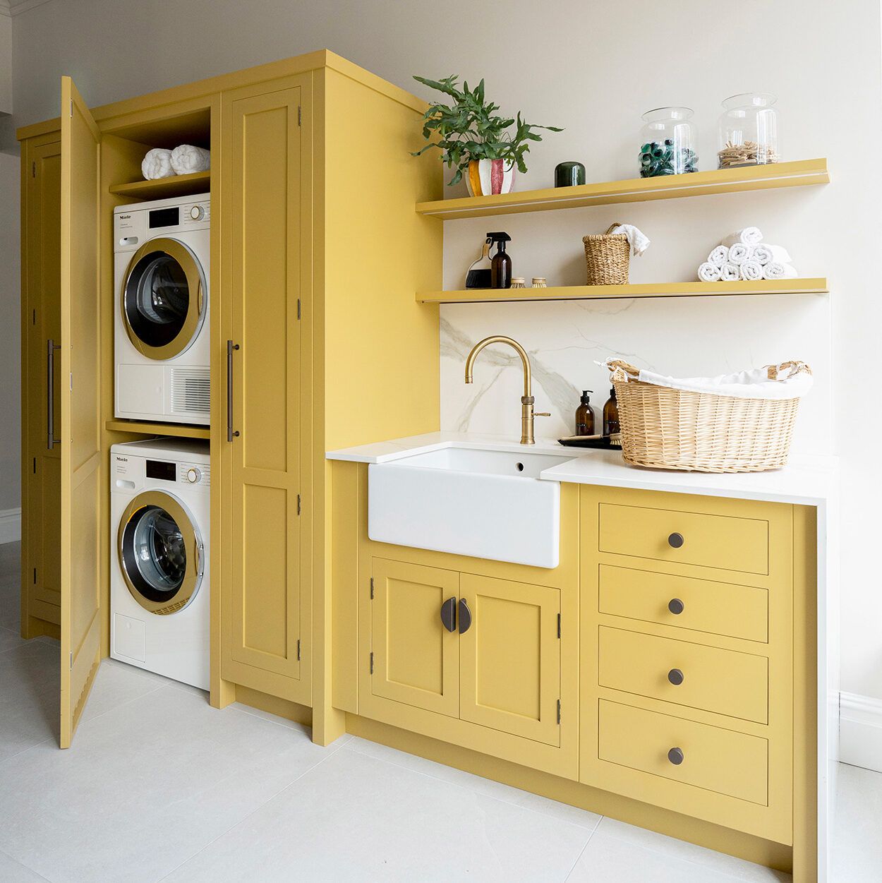Yellow utility room with stacked washer dryer, open shelving and Belfast sink
