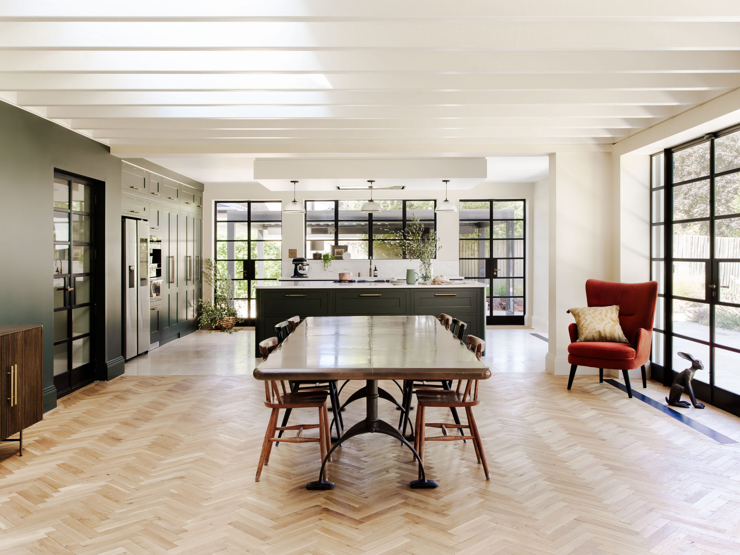 Open plan luxury kitchen with dark green cabinetry and large dining table