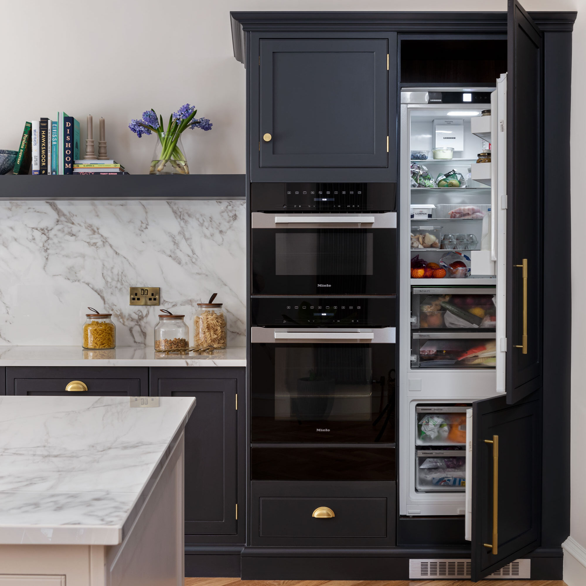 Dark kitchen with integrated luxury appliances and marble backsplash