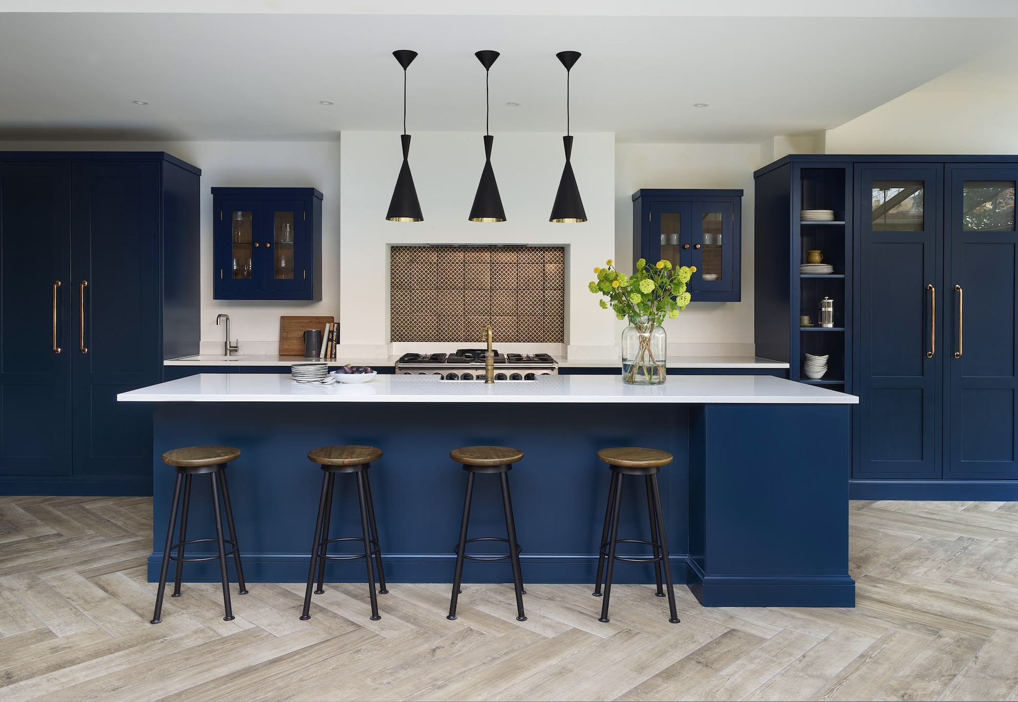 navy blue shaker kitchen with white quartz worktop and warm natural textures with wood accents, light wood flooring and brass hardware