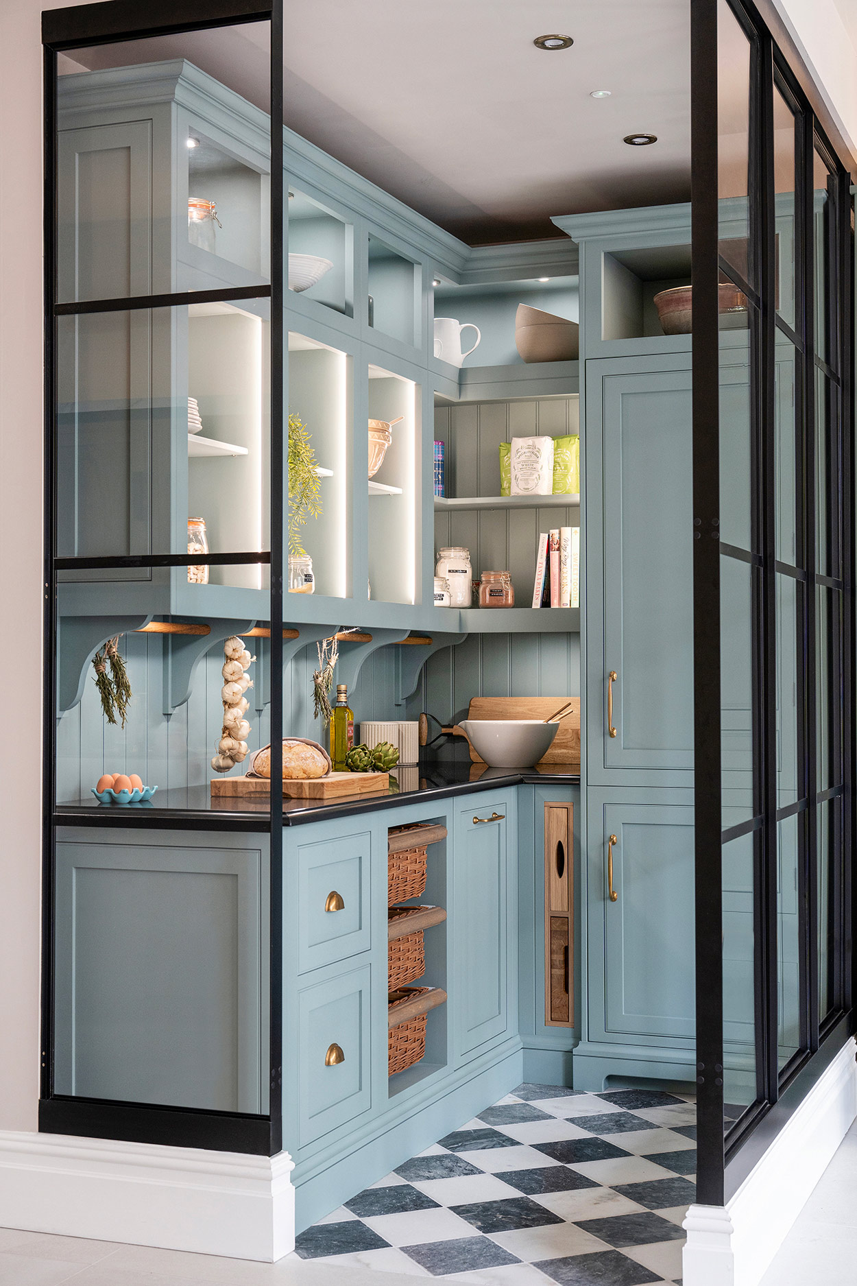 Walk in corner pantry with blue shaker style cabinetry, worktop space and lighting