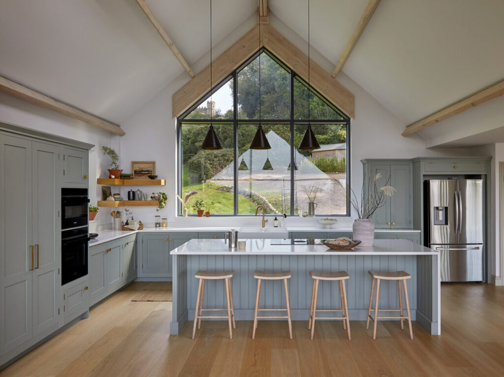 Light blue Shaker kitchen with L shaped layout in open plan design featuring wooden flooring and white quartz worktops