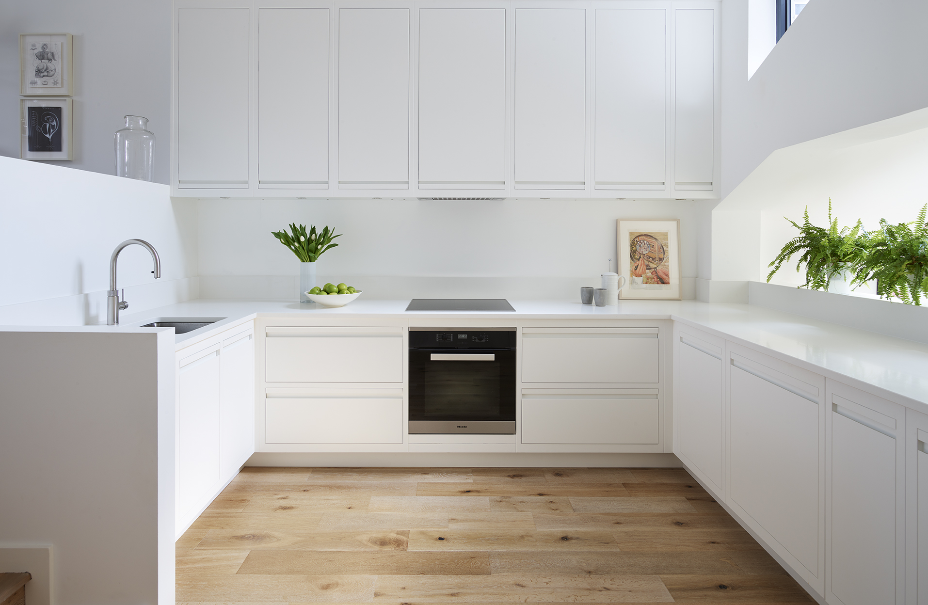 Clean white ultra modern kitchen with wooden flooring and U shaped layout for countertop space