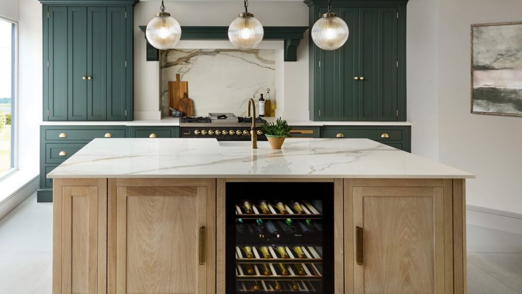 Two tone kitchen with dark green cabinetry and stained wood island featuring statement lighting, a wine fridge and marble worktops