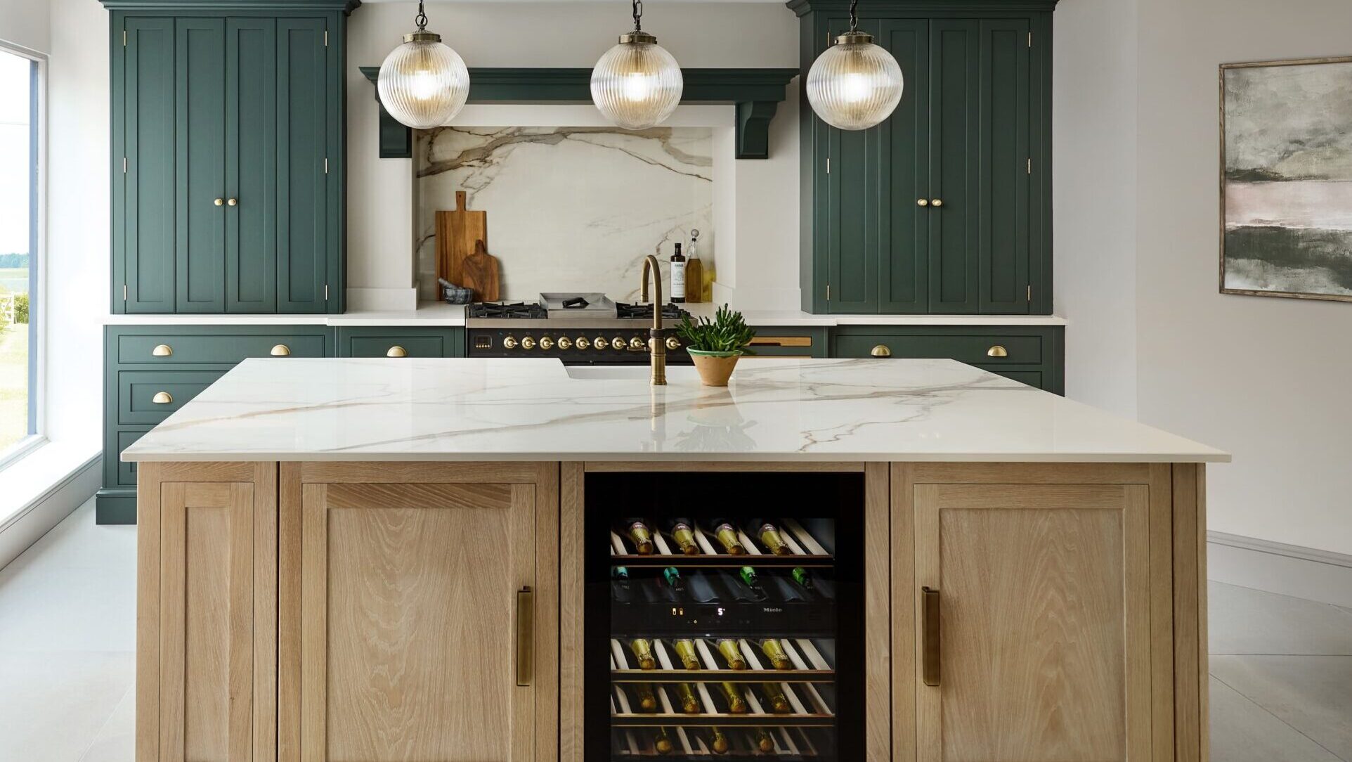 Two tone kitchen with dark green cabinetry and stained wood island featuring statement lighting, a wine fridge and marble worktops
