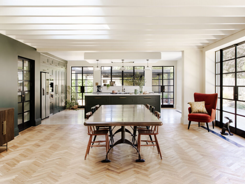 Open plan luxury kitchen with herringbone wood floor and large tiles defining zones through a change in material