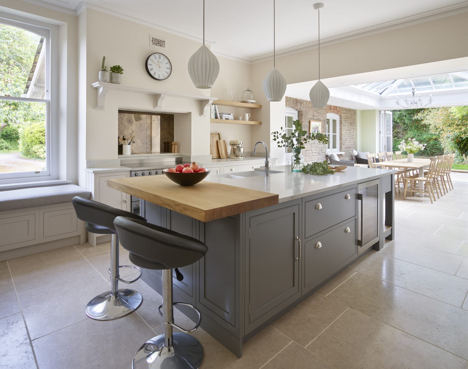 Grey kitchen island in an orangery kitchen extension with large dining table, pendant lighting and large format stone flooring