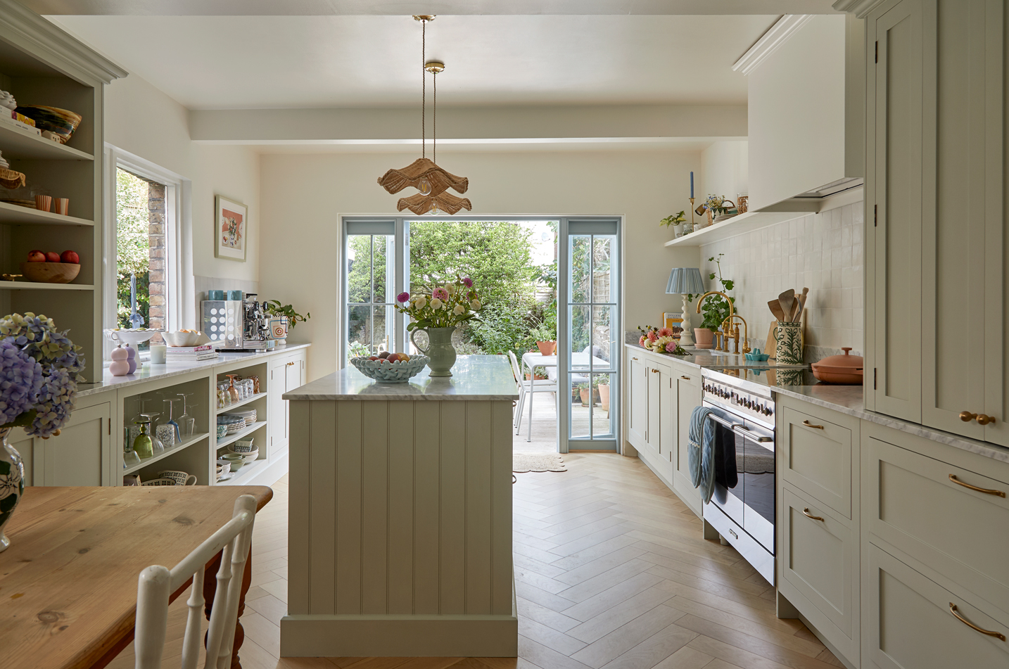 Sage green shaker kitchen with small kitchen island and warm natural accessories