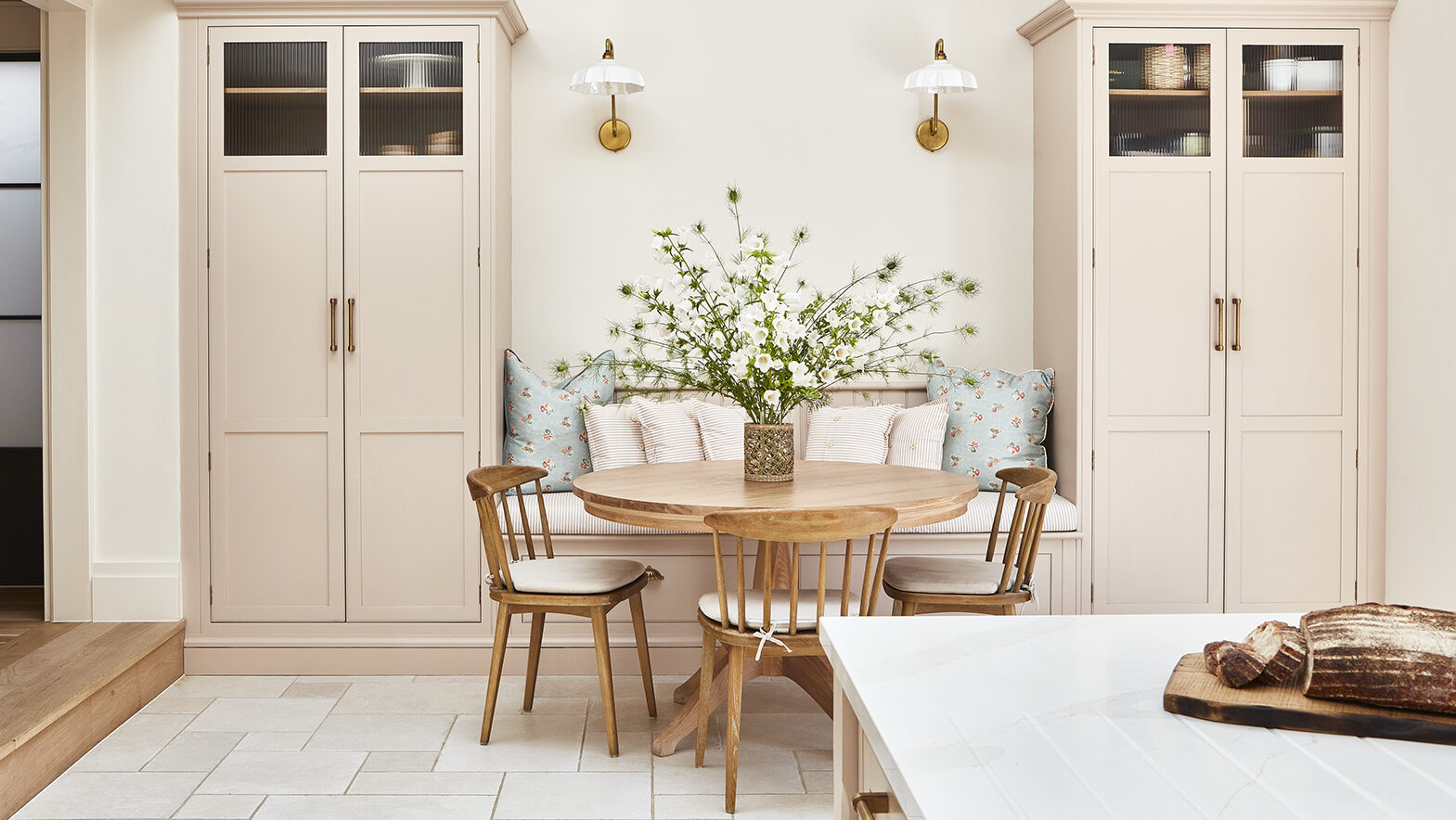 Breakfast nook in light pink kitchen diner with bespoke banquette seating and built in pantry cupboards