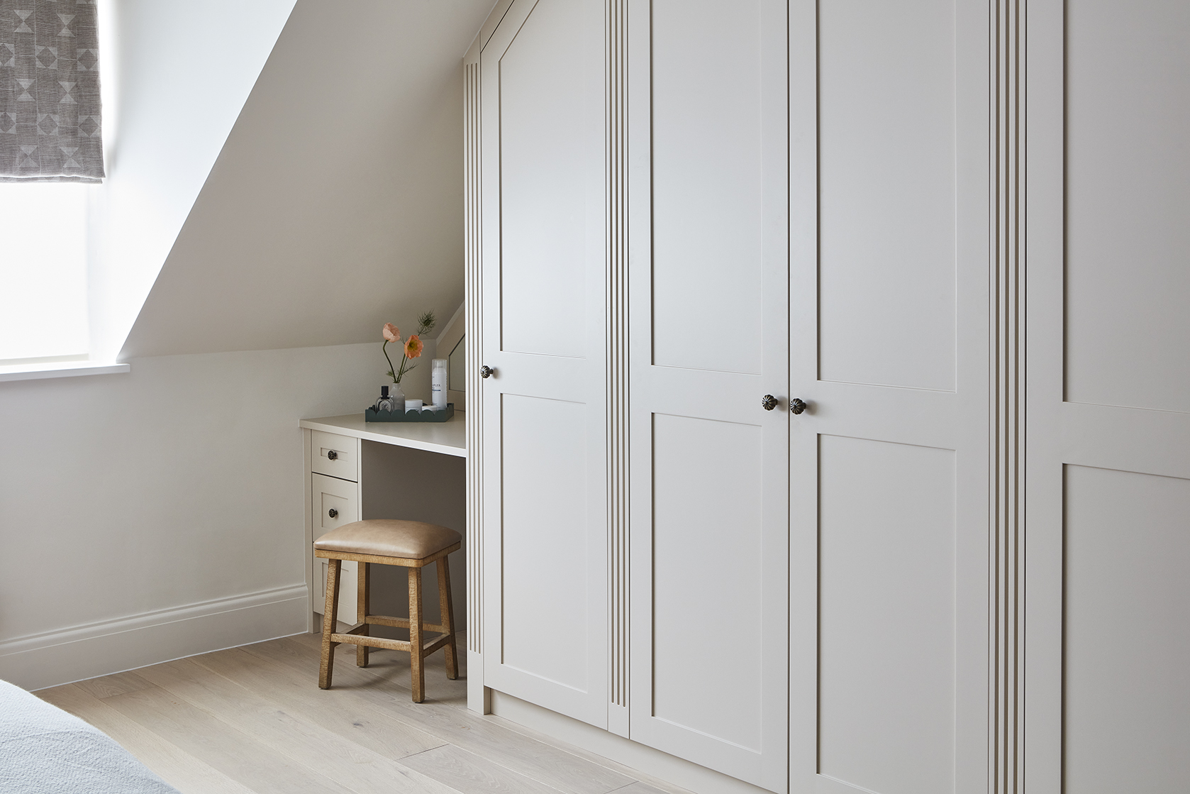 Small dressing room nook with stool and vanity space beside bespoke fitted wardrobes
