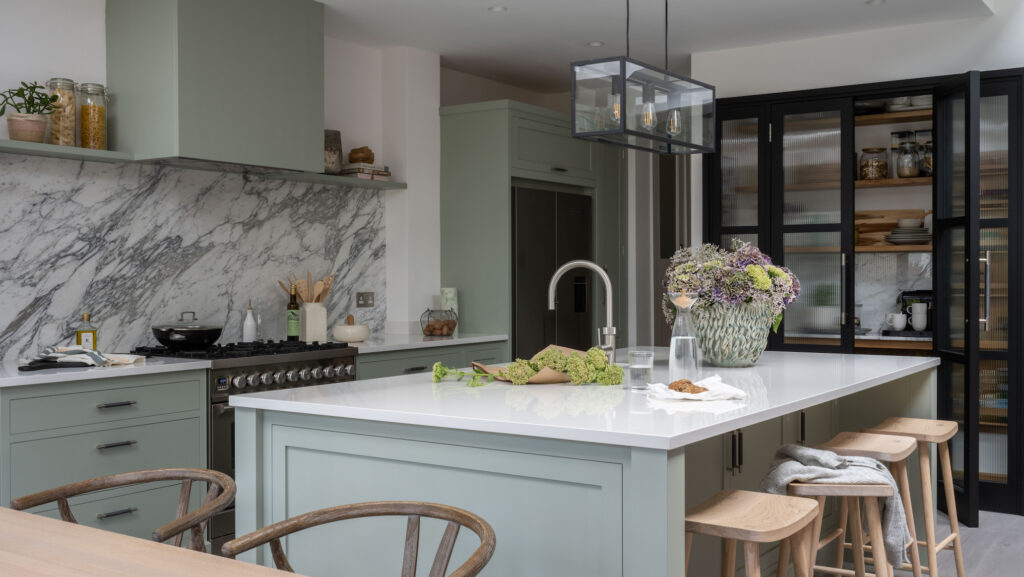 Light green modern kitchen with marble splashback and island and black glass fronted pantry doors