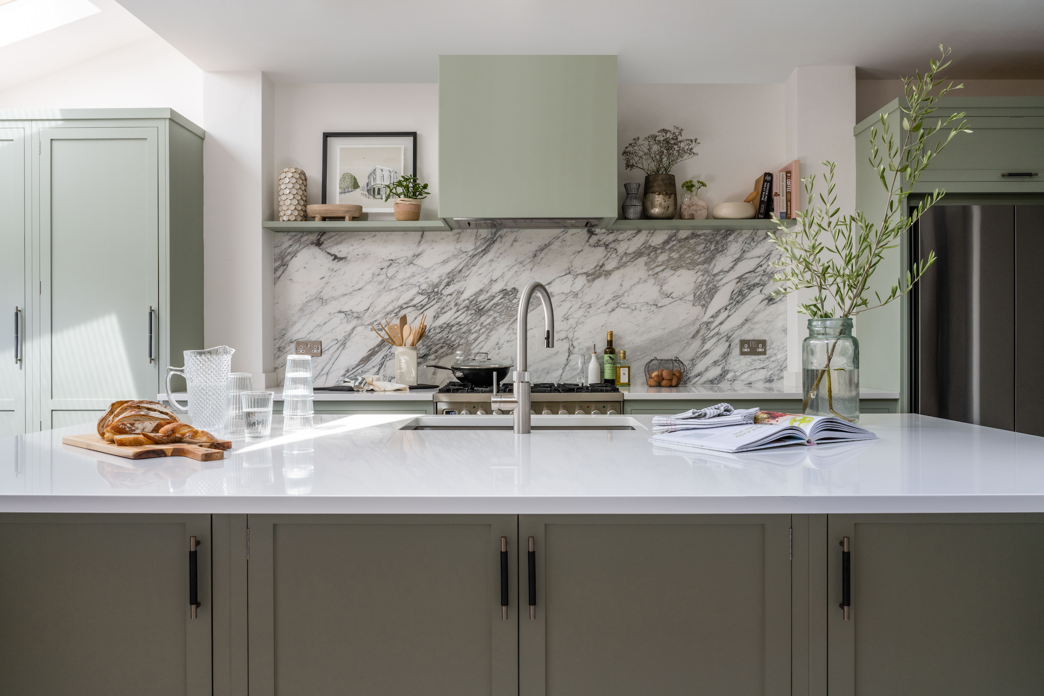 Light green kitchen with modern black accents and bold marble splashback
