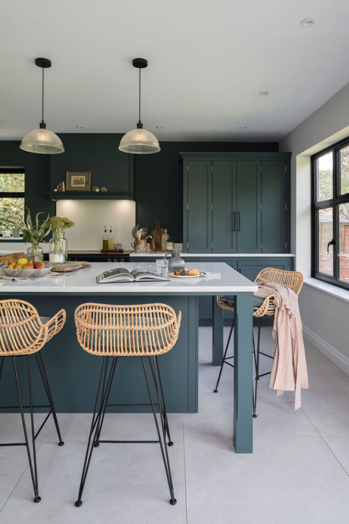 Dark green kitchen with island and quartz worktop with rattan island seats