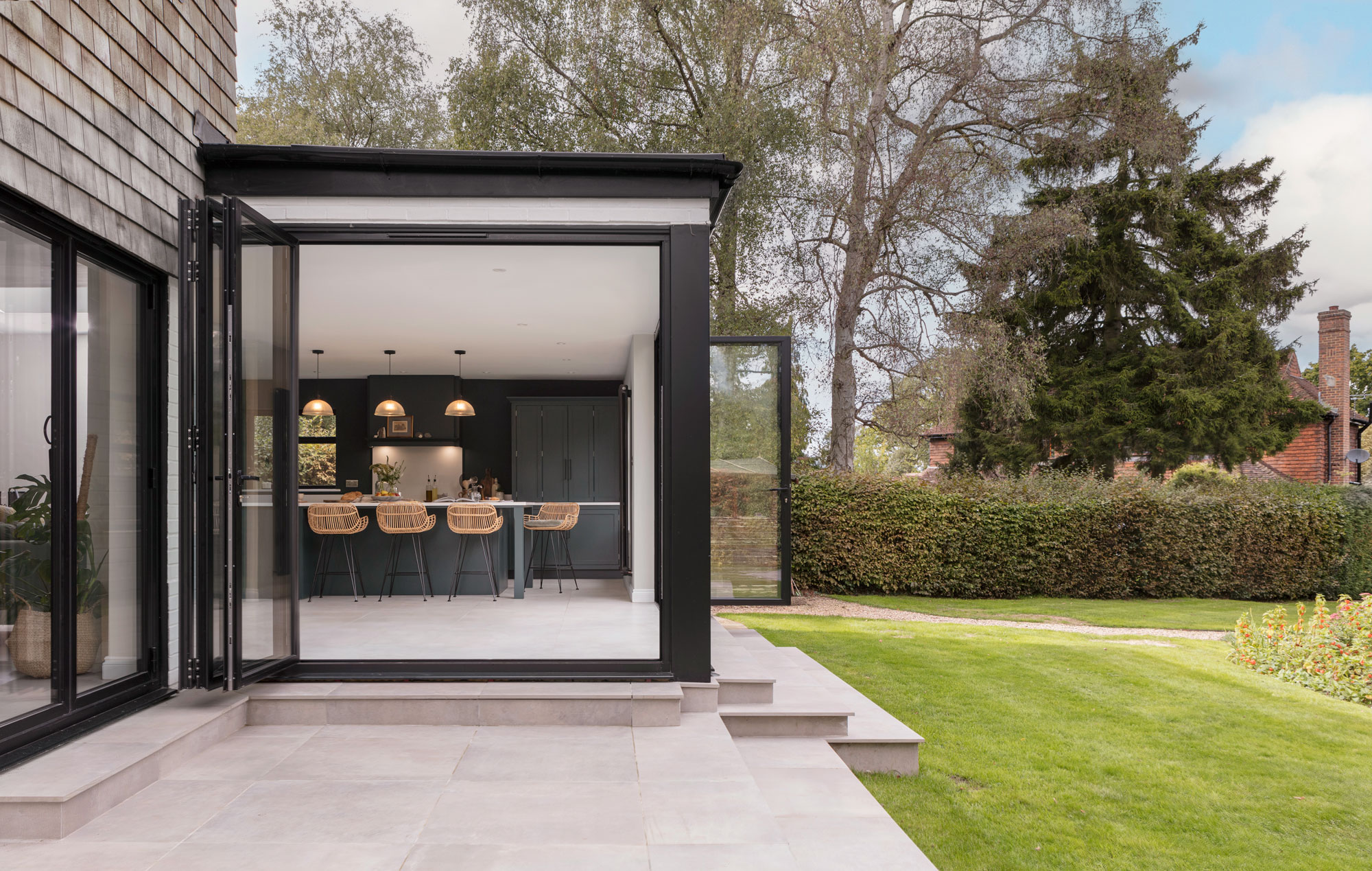 Navy blue modern kitchen in an orangery extension with rattan island seating and bifold doors