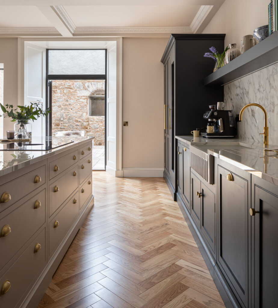 Wooden herringbone floor in a navy and neutral modern kitchen design with shaker style cabinetry and brass accents