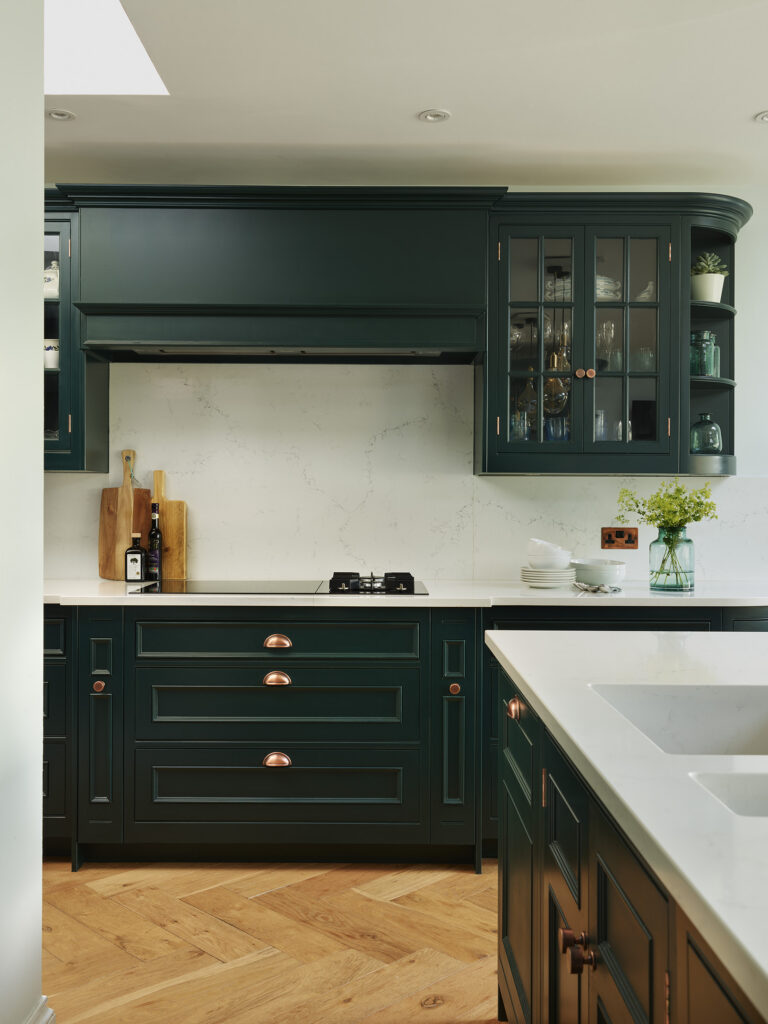 Dark green ornate in frame kitchen with gold hardware, herringbone wooden flooring and quartz worktops