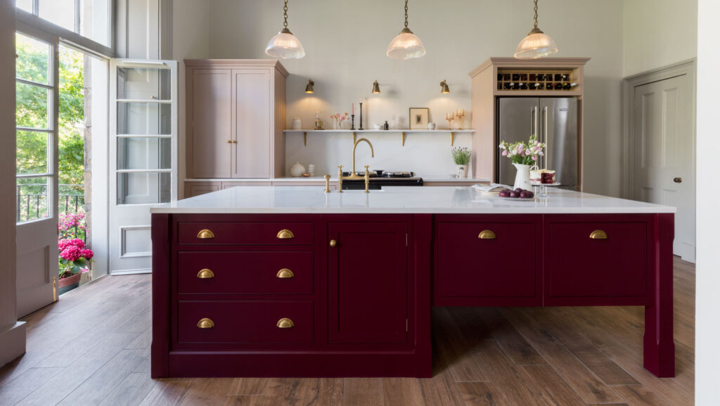 Burgundy and pink in frame kitchen with brass accents, wooden flooring and bespoke island
